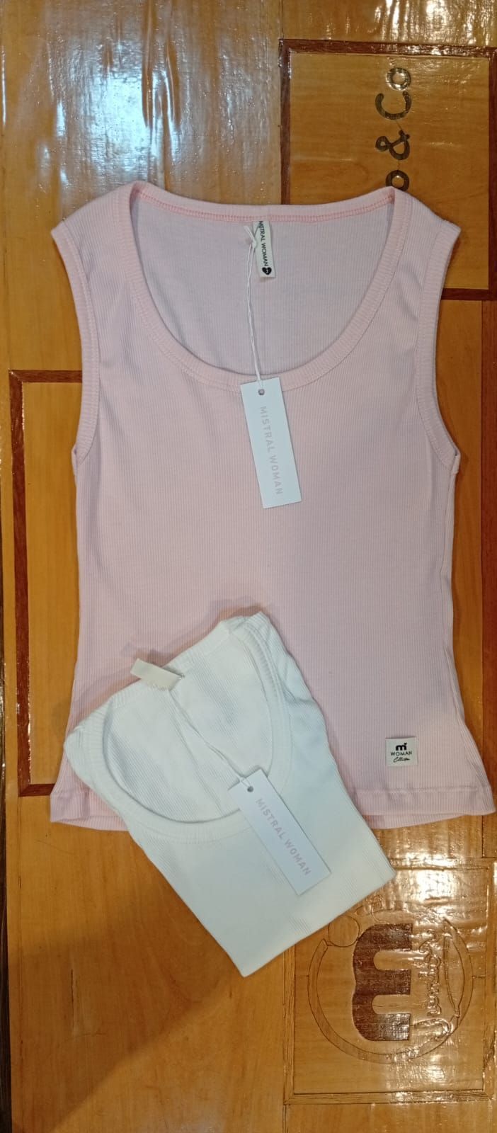 Una camiseta rosa sin mangas con una camisa blanca doblada debajo, sobre una superficie de madera.