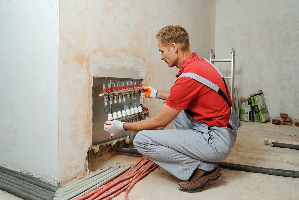 A Worker Holds The Underfloor Heating Manifold — Sydney Underfloor Heating in Woonona, NSW