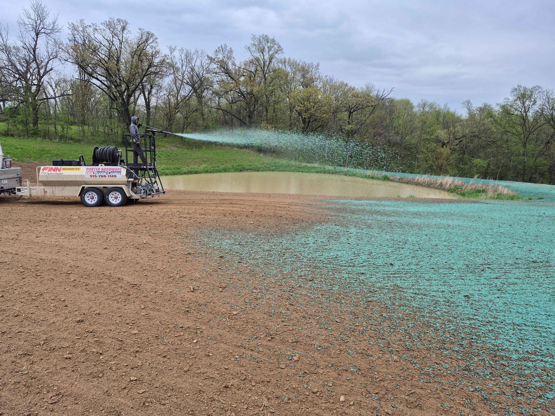 Farm field being sprayed with a green agricultural liquid from a tractor-mounted sprayer.