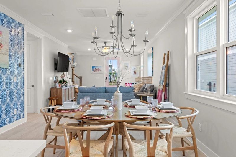 Dining room with a round table set for a meal, adorned with a chandelier and bright windows.