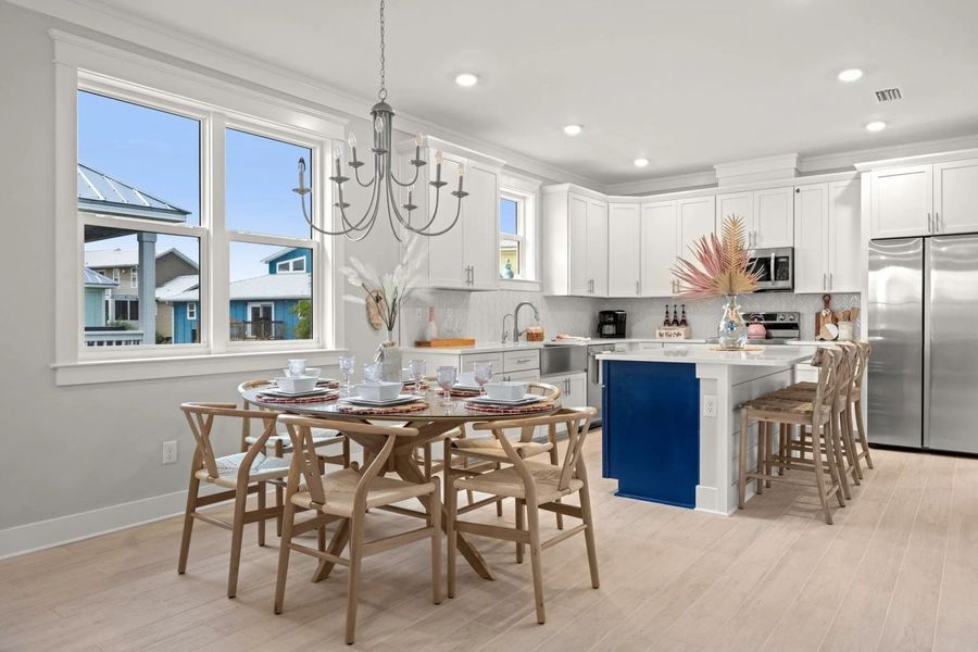 Open kitchen with dining area; white cabinets, blue island, wood table, chairs, chandelier, view of houses.