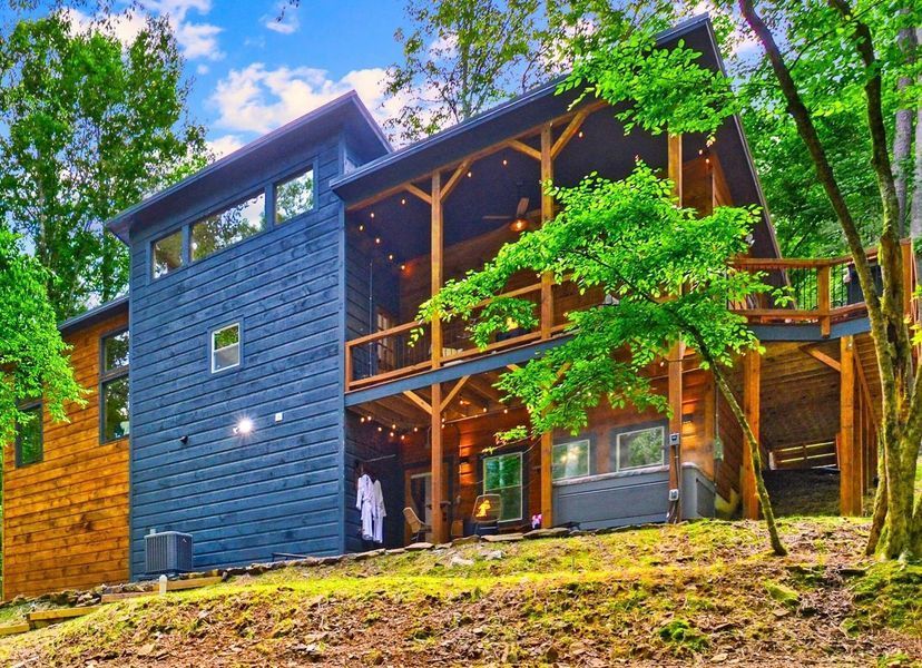 Two-story cabin nestled in the woods, blue siding, wooden deck, and string lights.