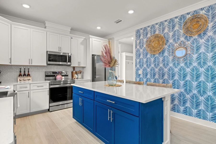 Modern kitchen with white cabinets, blue island, and patterned accent wall.