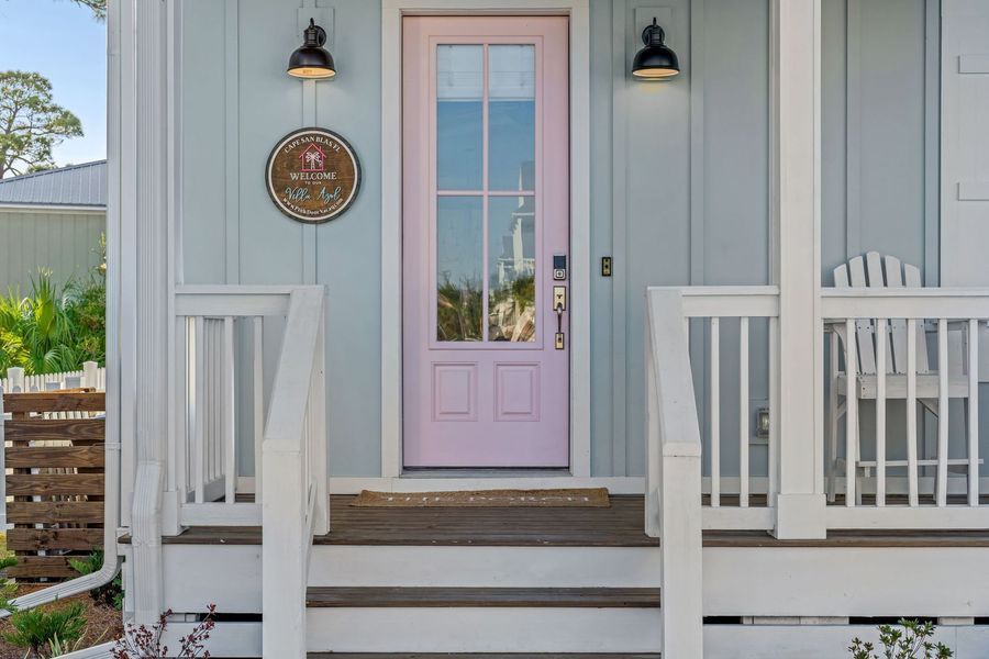 Light blue house with a pink front door, two black lights, and a small porch.