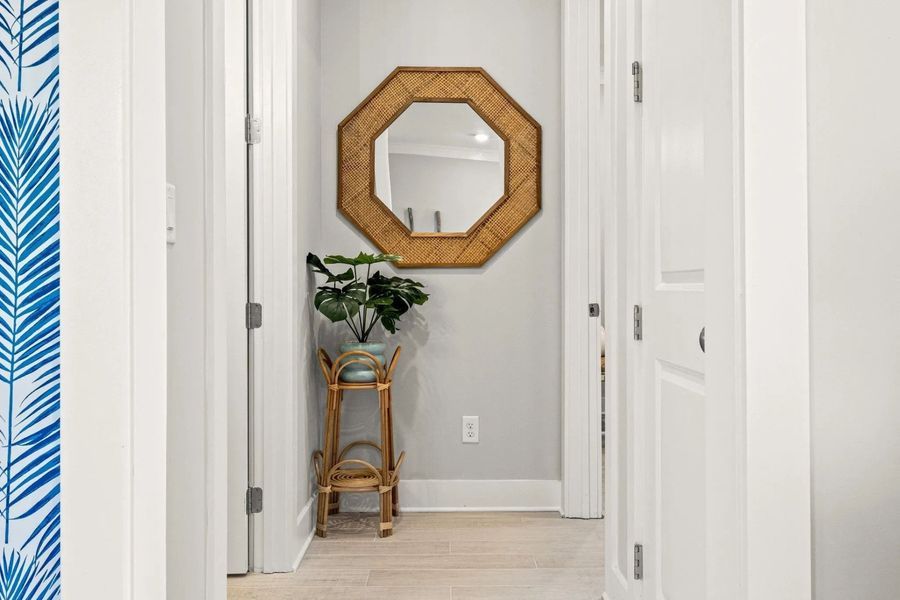 Hallway with octagonal mirror, plant on bamboo stand, and blue palm leaf wallpaper.