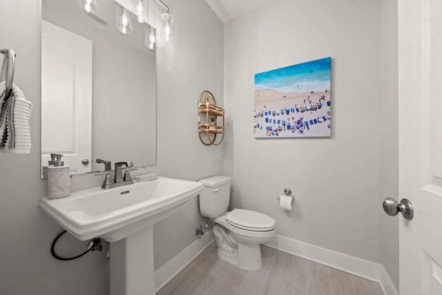 Powder room with pedestal sink, toilet, and beach art on a gray wall.