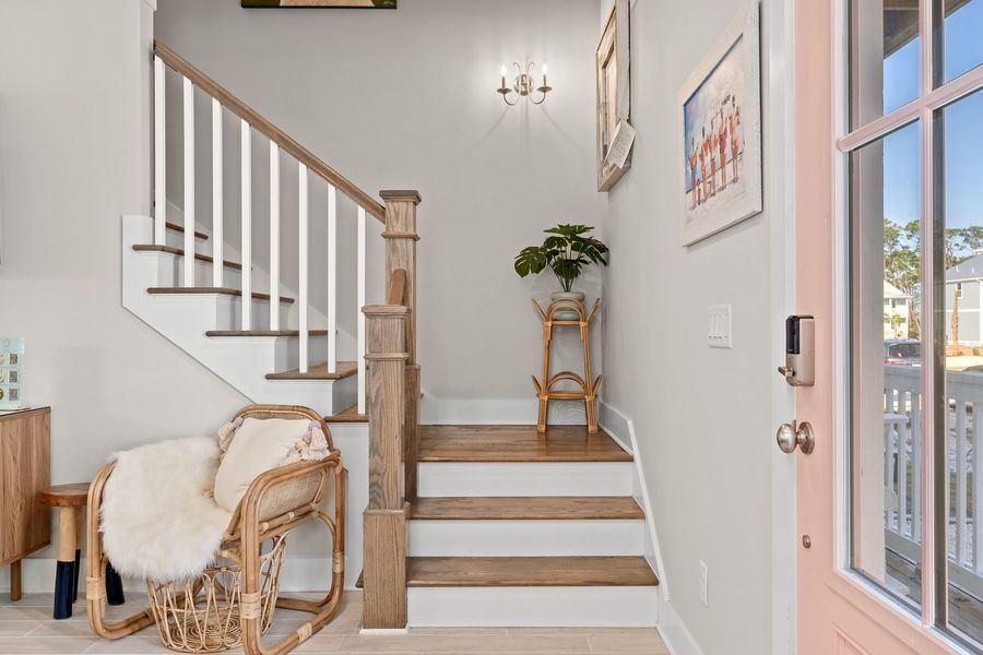 Entryway with a staircase, chair, and plant. Light gray walls, natural wood accents, and a pink door.
