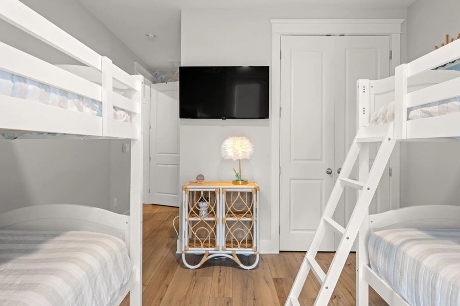 Bedroom with two white bunk beds, a TV, and a nightstand with a lamp.