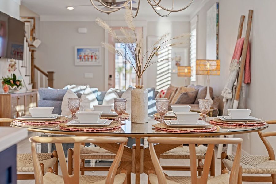 Dining room with a glass table set for six, vase with dried flowers, view to a living area.