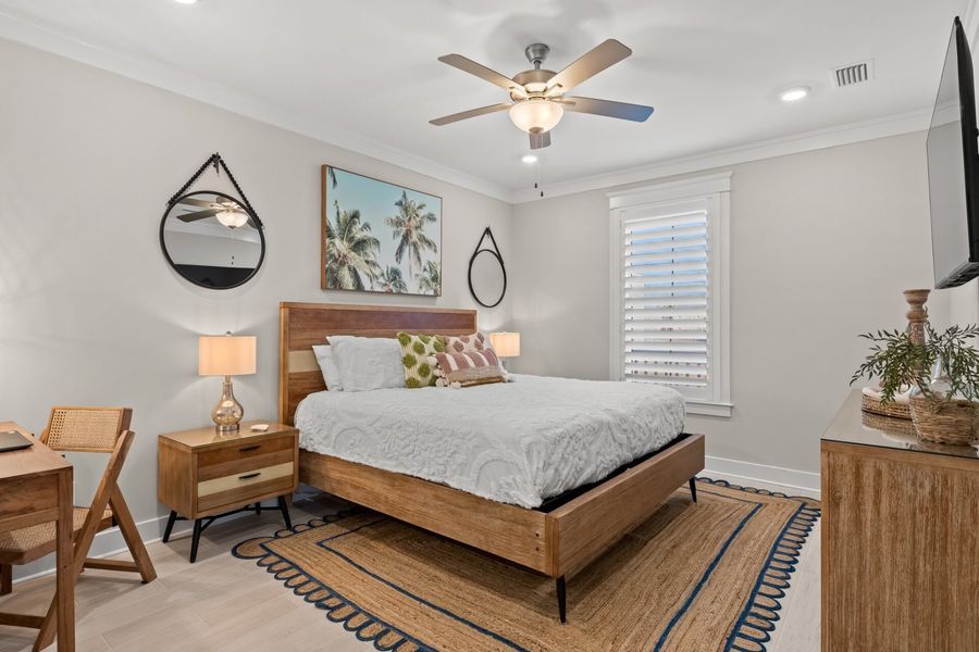 Bedroom with bed, desk, mirrors, and palm tree art. Earth tones and neutral walls.