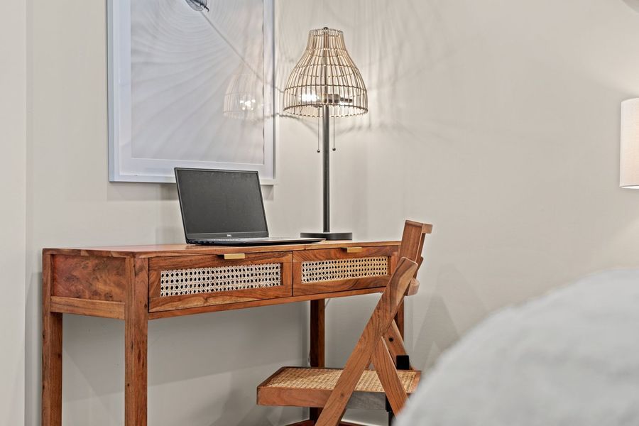 Wooden desk with laptop, lamp, and chair in a bedroom.