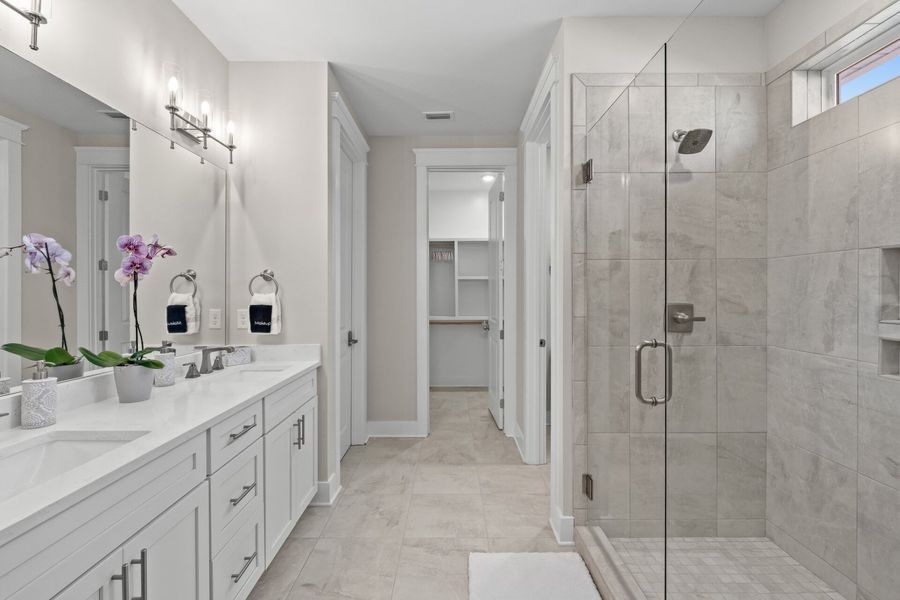 Bright white bathroom with double vanity, walk-in shower, and closet; neutral gray tile.