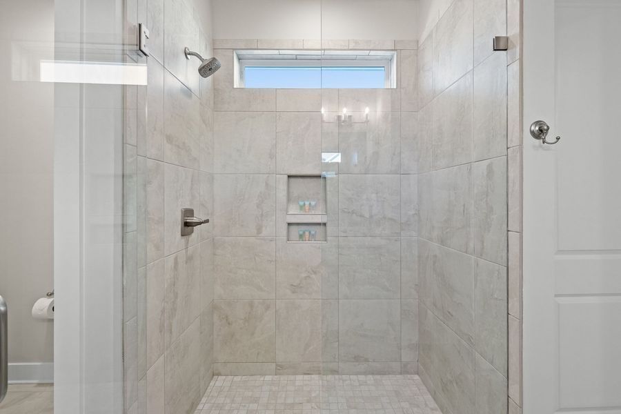 A modern bathroom with a tiled shower, glass door, and recessed storage.