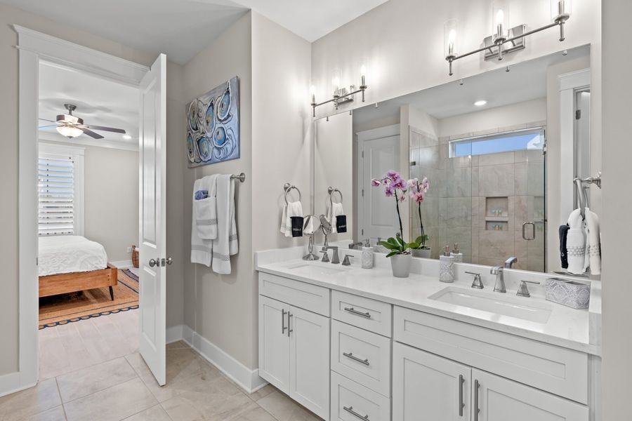 Bathroom with white double vanity, open door to bedroom, and large mirror.