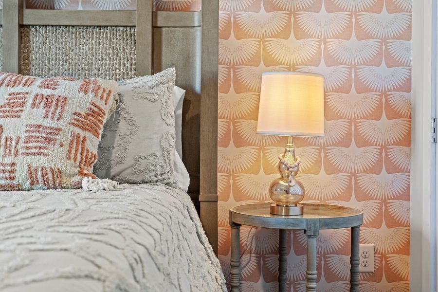 Bedroom with bed, patterned wallpaper, nightstand, and lamp.
