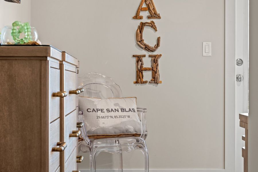 A tan dresser, clear chair with pillow, and decorative letters spell 