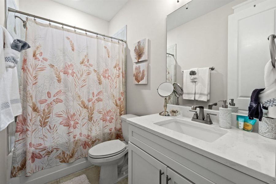 Bathroom with white vanity, toilet, and shower with floral curtain.