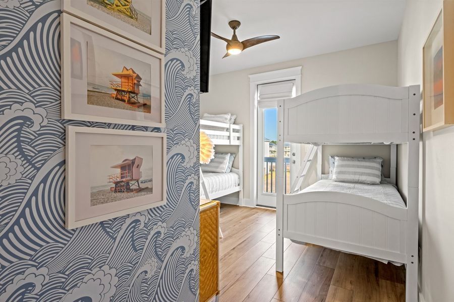 Bedroom with white bunk beds, wave wallpaper, and framed beach art.