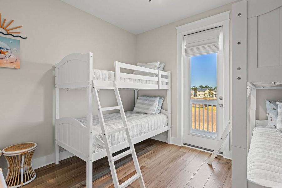 White bunk beds in a bedroom with a door to an outdoor view; wood floors.