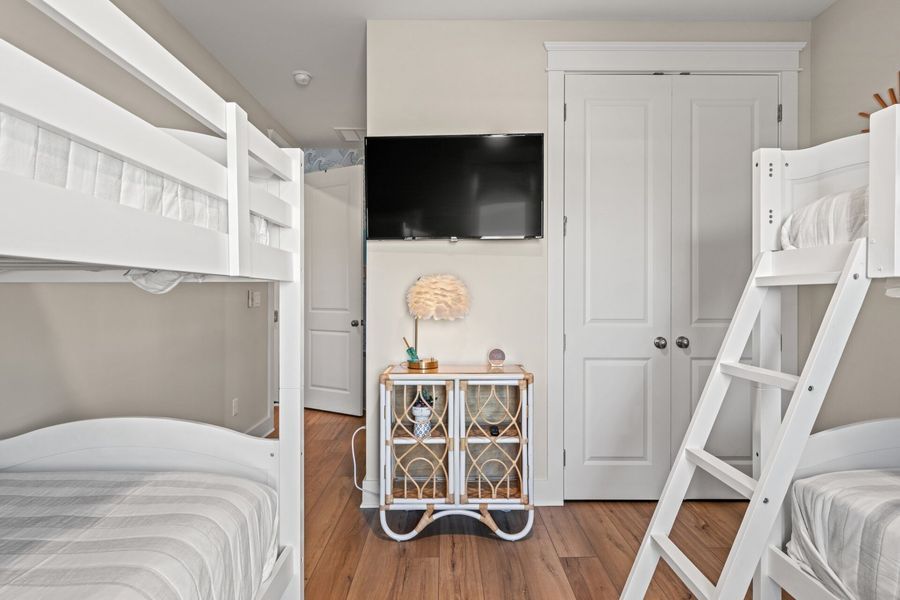 Bunk bed room with white furniture, TV, and small cabinet on hardwood floors.