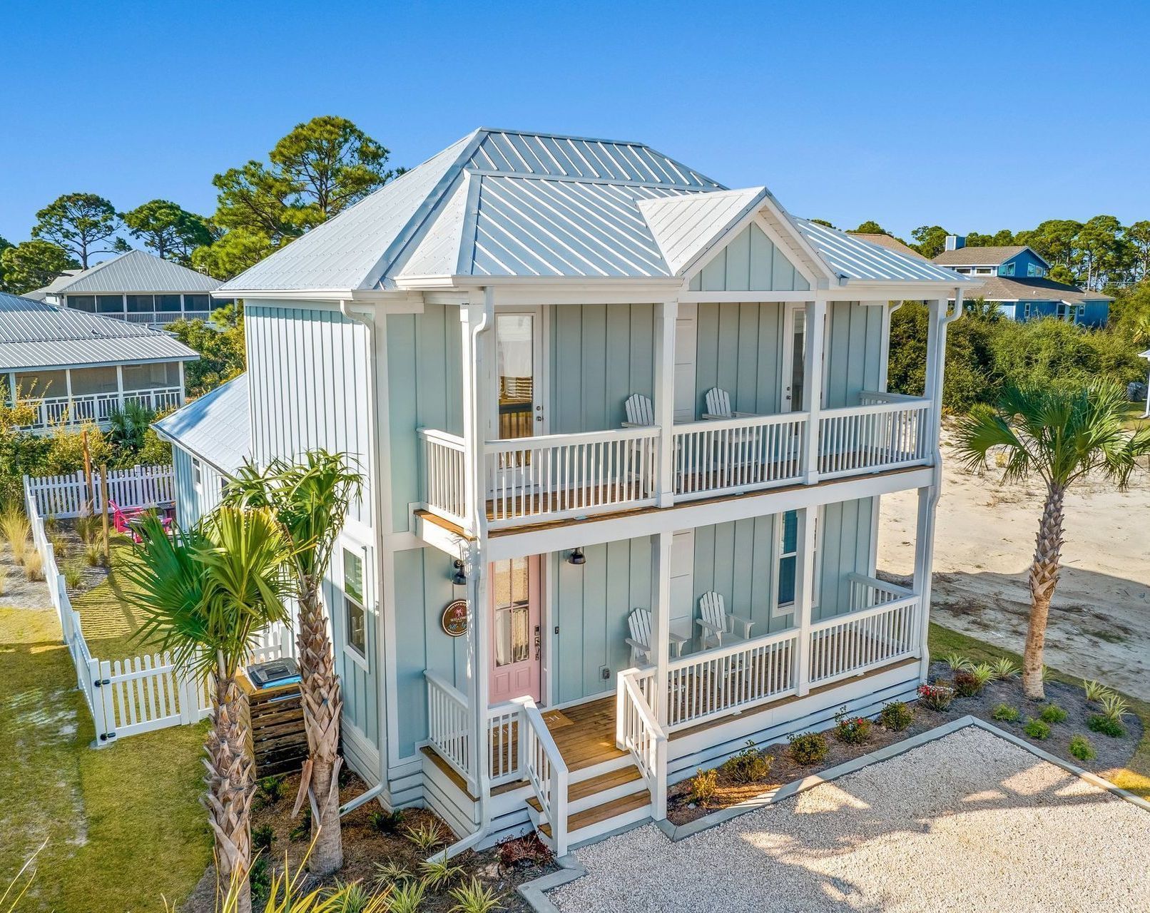 Two-story light blue beach house with white trim, balconies, and palm trees.