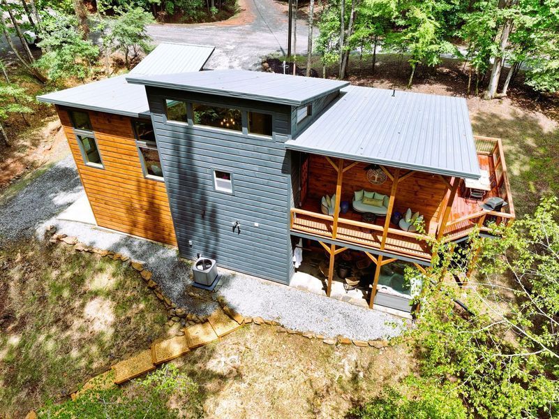 Modern cabin with wood and gray siding, metal roof, and a deck in a wooded setting.