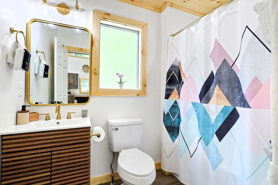 Small bathroom with a mountain-patterned shower curtain, gold fixtures, and a wooden vanity.