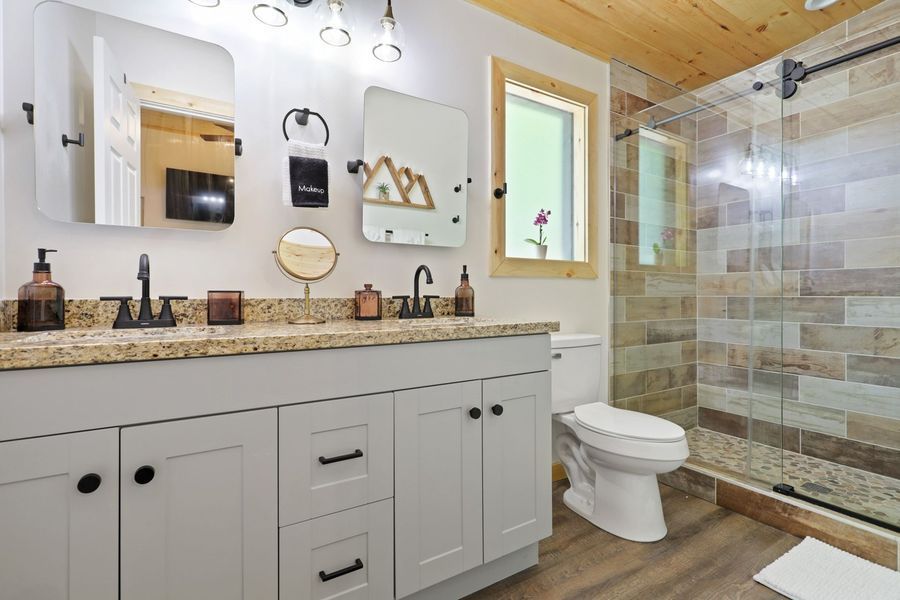 Bathroom with double vanity, shower, and toilet; neutral color scheme, wood accents.