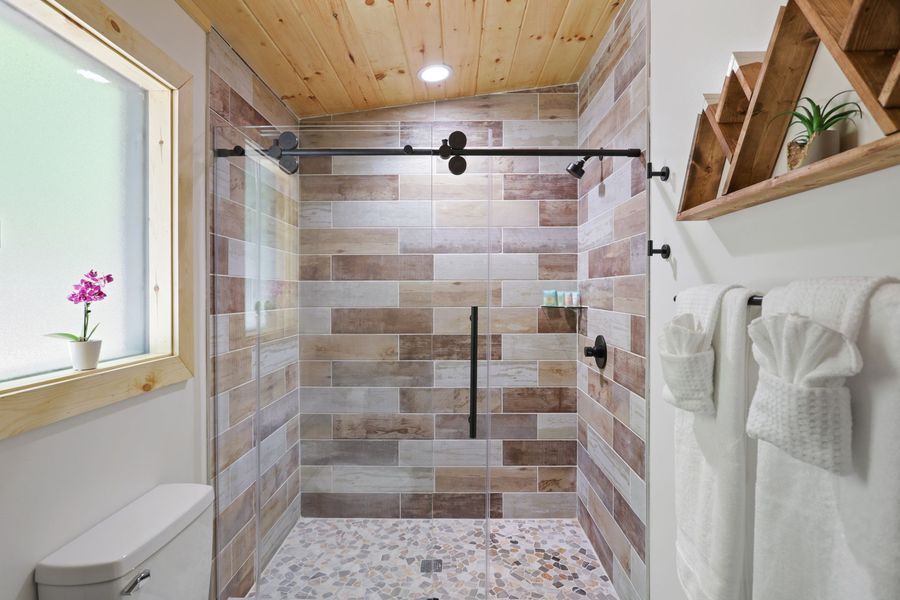 Rustic bathroom with wood ceiling, stone tile shower, and white towels.
