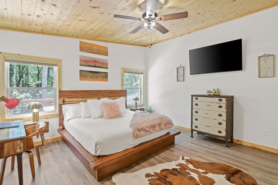 Bedroom with wooden bed, dresser, TV, and cowhide rug; light wood ceiling and flooring.