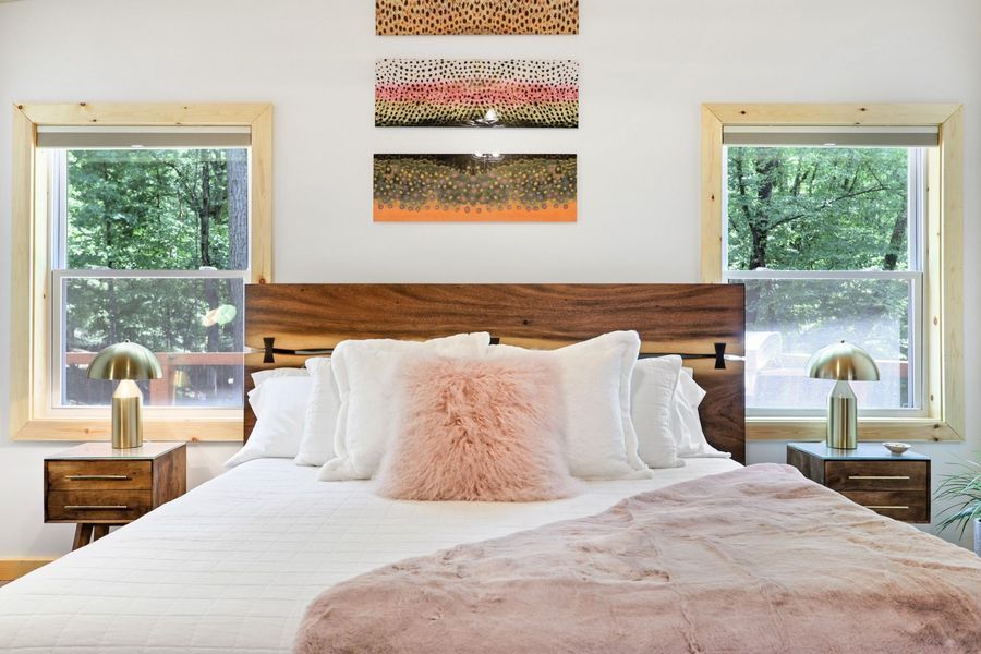 Bedroom with a wooden headboard, windows, nightstands, bed with pink accents, and abstract art.