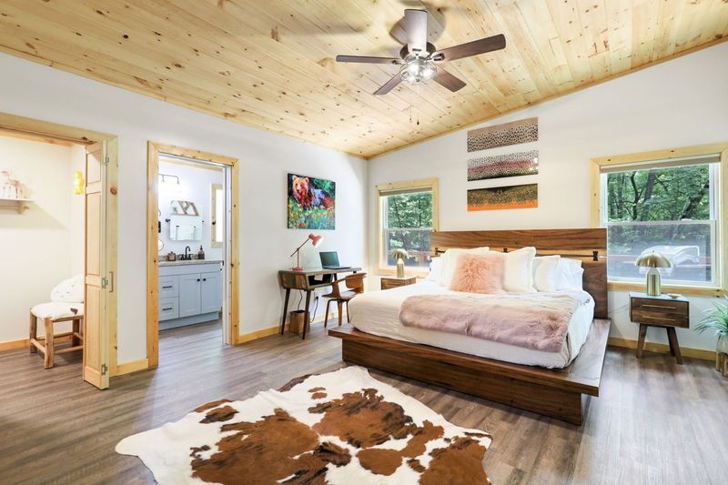 Bedroom with wooden ceiling and floors, a bed, desk, and doorway to a bathroom.