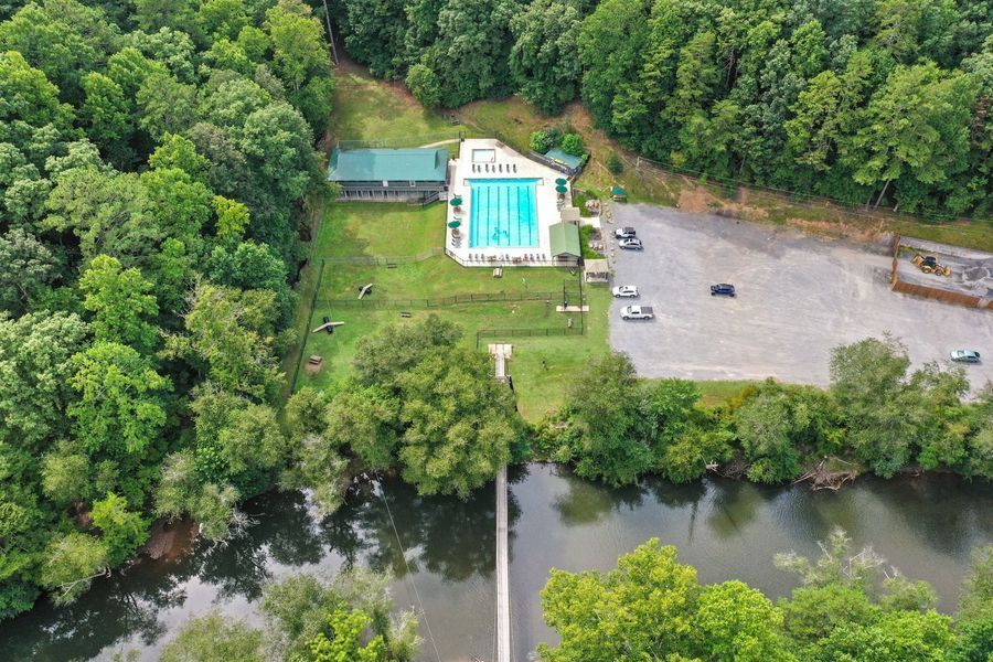 Aerial view: Pool and building surrounded by trees, a bridge over a river, and a parking area.