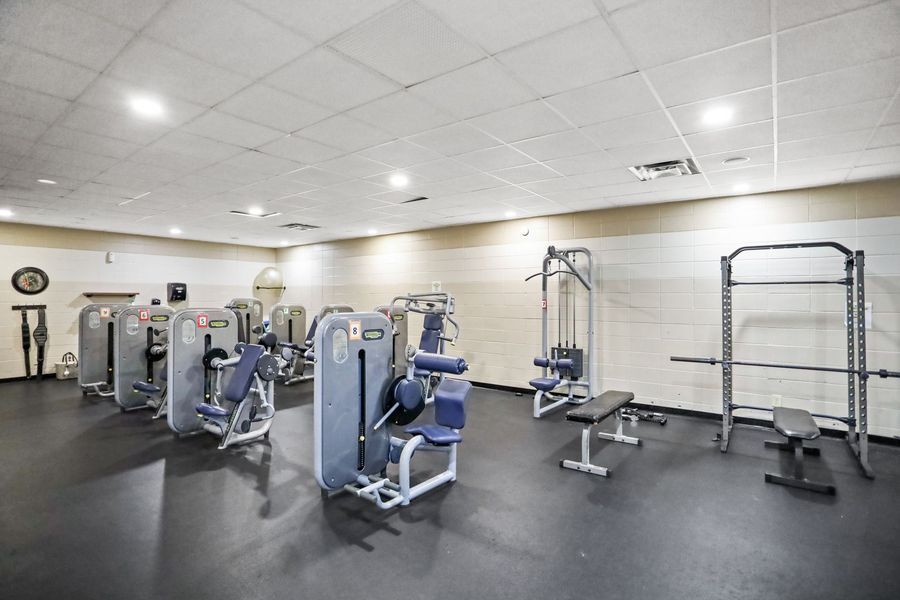 A fitness gym with various weight machines, weights, and a rack on black flooring.