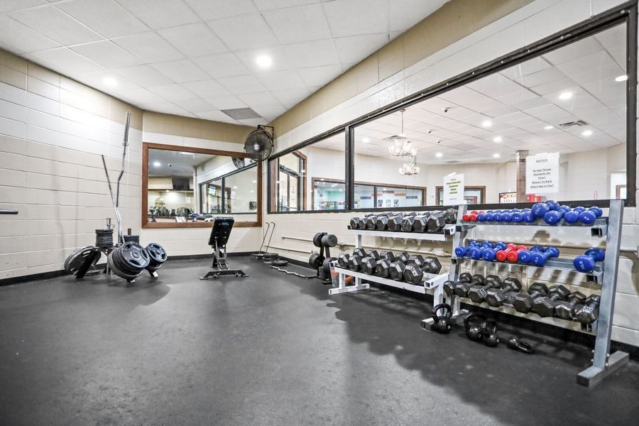 Gym interior with weights, rowing machine, and mirrors.