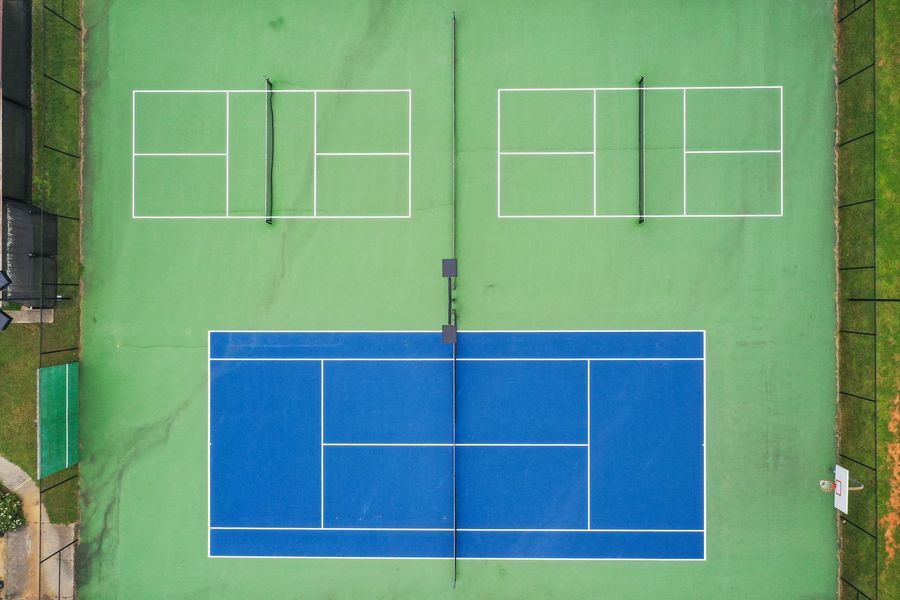 Overhead view of pickleball and tennis courts; two green courts, one blue court, nets, and a fence.