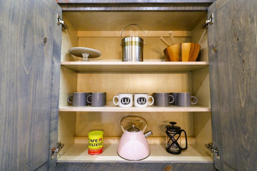 Open cabinet with kitchen items on shelves: mugs, kettle, utensils, and containers.