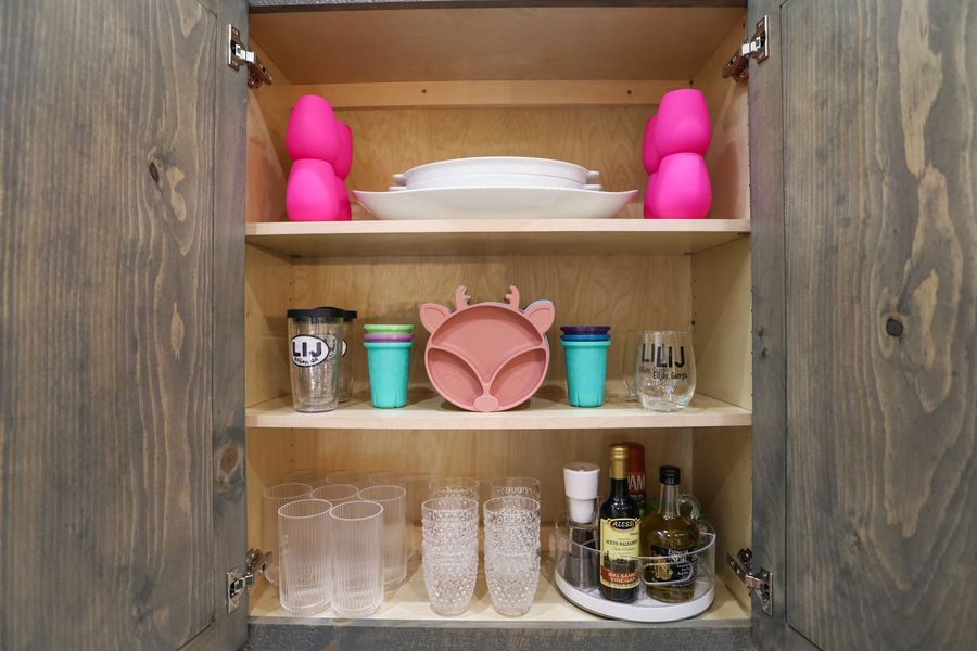 Kitchen cabinet organized with dishes, cups, and bottles in a gray wooden cabinet.