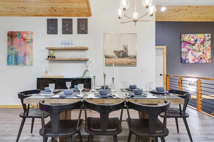 Dining room: Rustic wood table set for six, black chairs, art on white walls, wood ceiling.