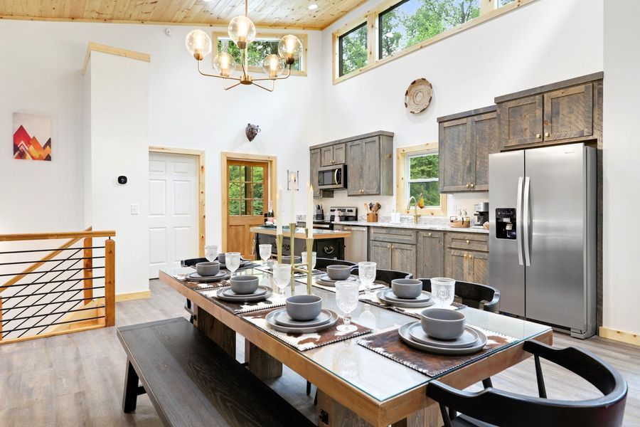 Dining area with a long table set for a meal, open kitchen with grey cabinets, tall ceiling, and skylight.