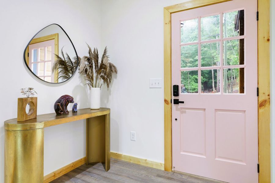 Pink door with glass panels in a white-walled entryway, gold console table, and a large mirror.