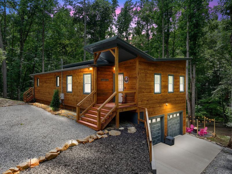 Wooden cabin with a gray gravel driveway and two-car garage in a wooded area.