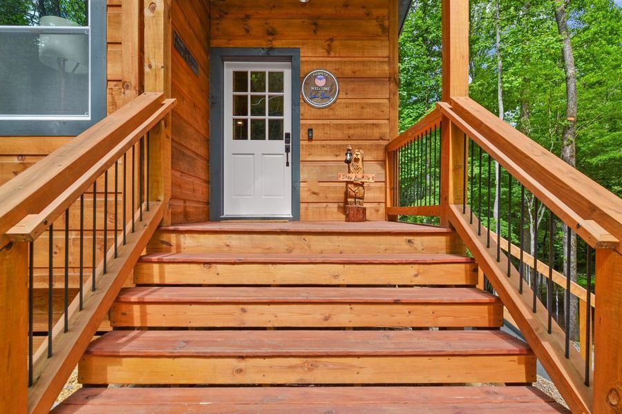 Wooden steps leading up to a white door of a cabin, with wooden railing and a wooded background.
