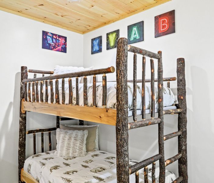 Bunk beds with rustic log framing, white walls, wood ceiling, and neon letters spell 