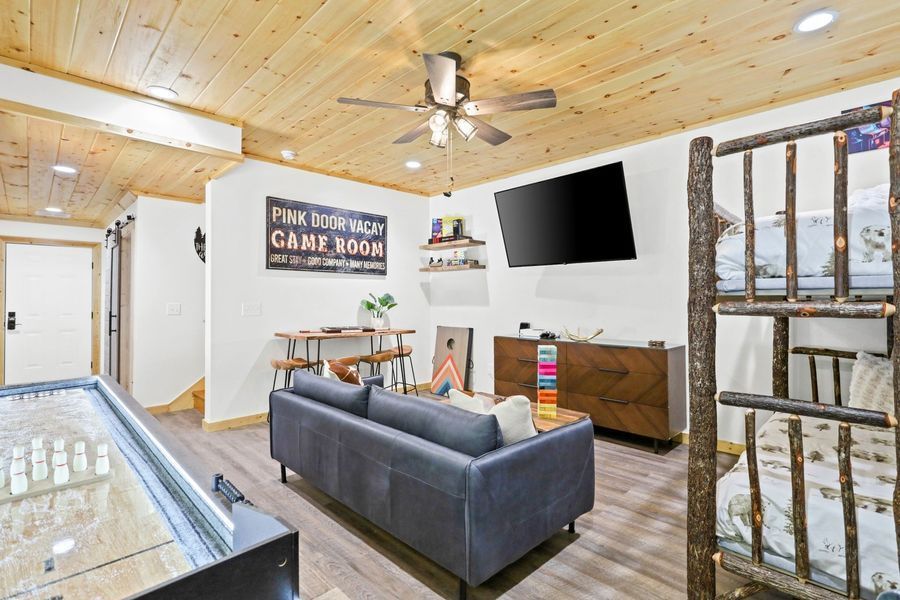 A cozy cabin game room with a shuffleboard, TV, sofa, bunk beds, and rustic decor.