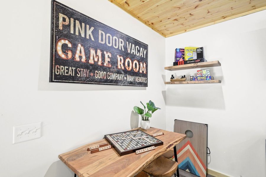 Game room with wooden table, sign, shelves, and a cornhole board.
