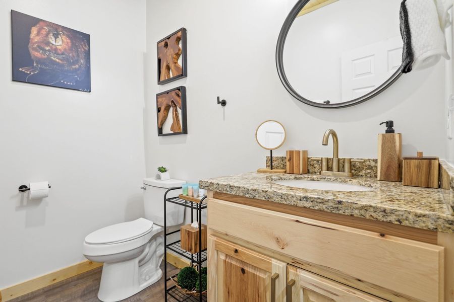 Bathroom with wood vanity, granite countertop, round mirror, and toilet; neutral colors.