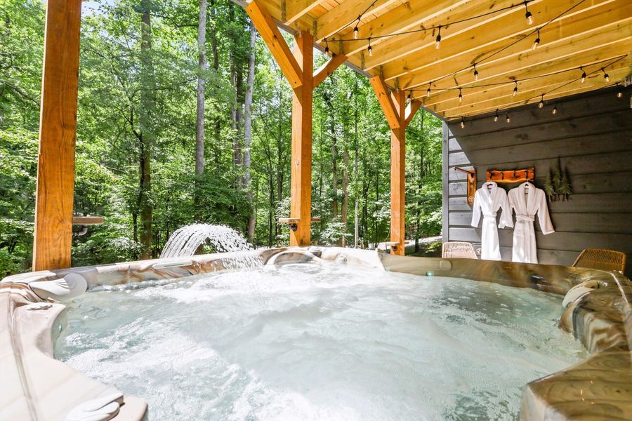 Hot tub with waterfall feature, wooden deck, robes hanging, set in a wooded area.