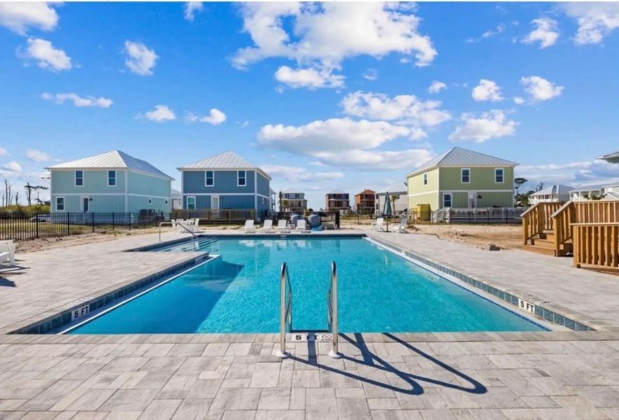 Swimming pool in front of pastel-colored beach houses on a sunny day.