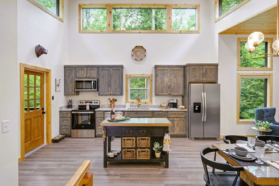 Rustic kitchen with wooden cabinets, stainless steel appliances, island, and large windows.